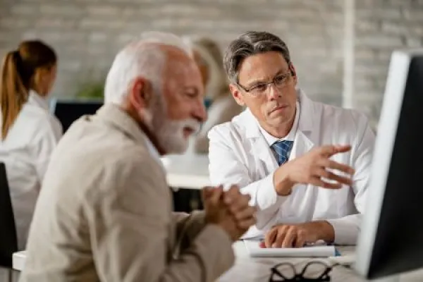 Serious doctor and mature patient examining medical data on computer during a meeting.