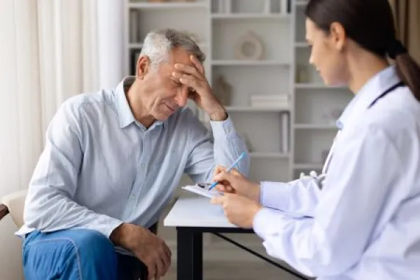 Senior male patient experiencing headache while female doctor records symptoms