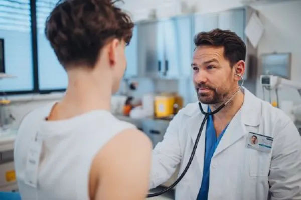 Cardiologist examining adolescent patient with stethoscope in clinic.