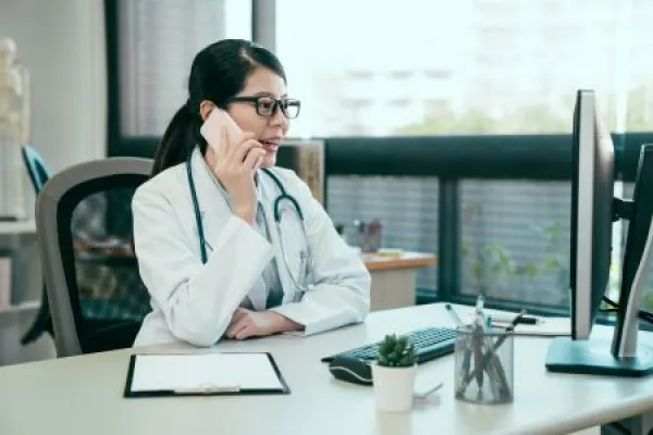 young asian female doctor using mobile phone talking while sitting in hospital office.