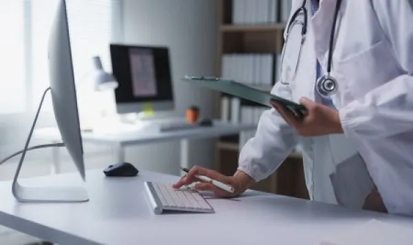 Female physician using computer keyboard and holding patient medical records in bright modern clinic