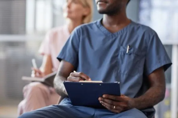 Cropped shot of African American man in blue scrubs keeping records of meeting on clipboard