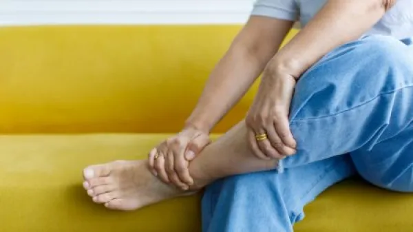 Woman sitting on sofa using hand to hold leg and feeling pain, suffer, hurt and tingling.