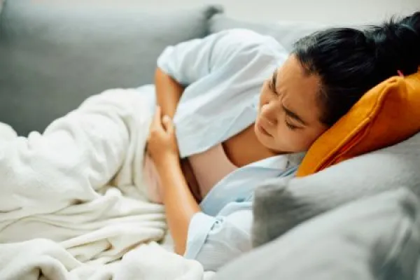 Young Asian woman suffers from stomachache while lying down on sofa at home.