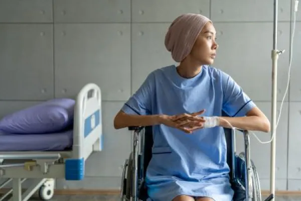 A cancer patient sits in a wheelchair with an IV drip looking stressed and sad.