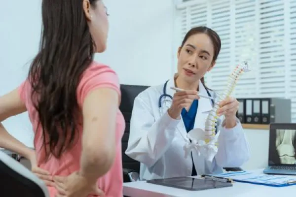 Doctor explains spine surgery using anatomical model, explaining symptoms and treatment to patients.