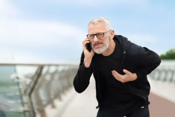 Senior sportsman touching left side chest, calling ambulance