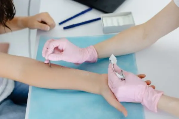 Doctor doing skin allergy test at white table in office.