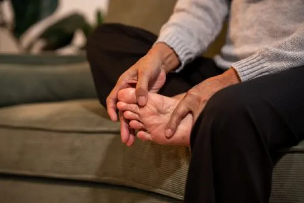 Close view of a senior woman sitting on a sofa and massaging her painful foot at home