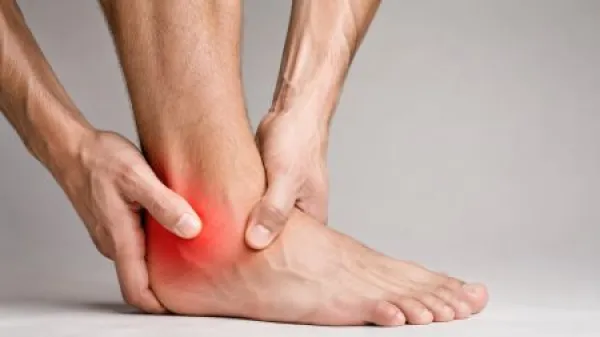Close-up of a male hand gripping an inflamed ankle with red pain area, indicating acute ankle pain, injury or medical care