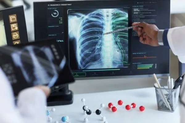 Doctors reviewing chest X ray on medical monitor, pointing at lung scan data for diagnosis and treatment planning.