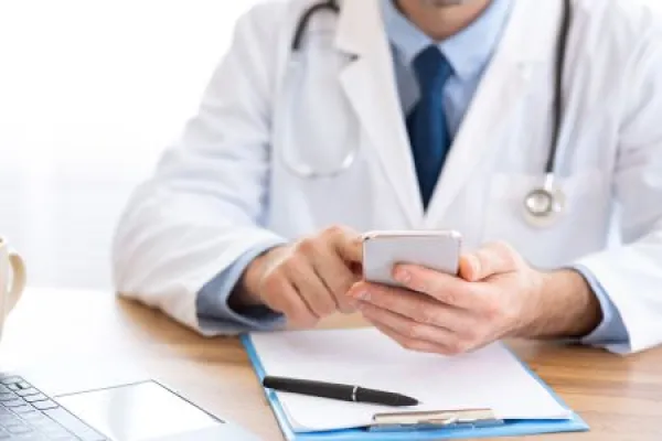 Doctor using smartphone at workplace, messaging with patient 